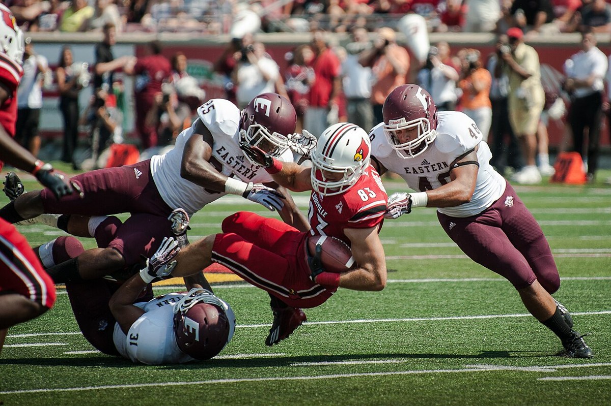 Louisville tight end Ryan Hubbell fighting for yardage against Eastern Kentucky on September 7, 2013. Archival team-action photo; the players shown are not presented as 2026 participants.